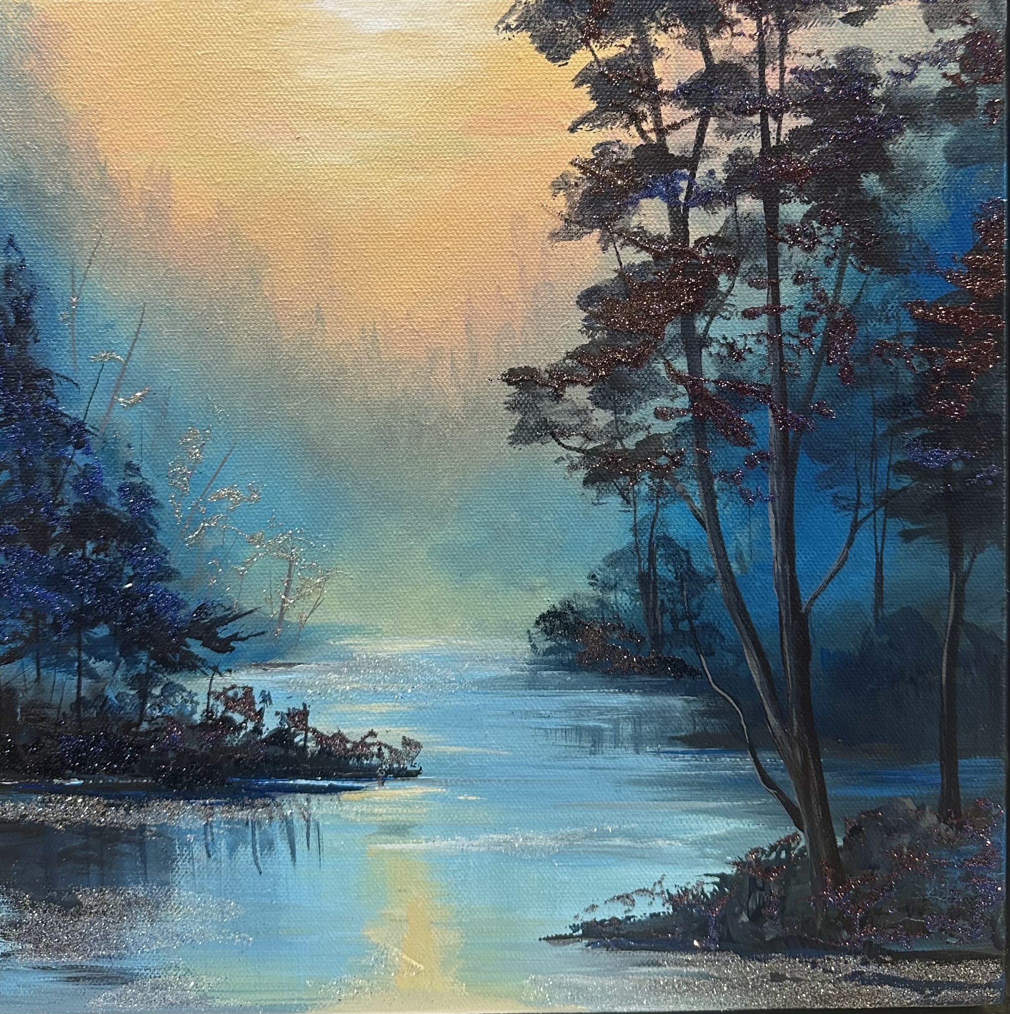 Golden Hour A 12x12 mixed-media landscape titled Golden Hour showing a warm sunset over a blue river, with trees framing the scene and subtle sparkle from gemstones, glass glitter, and mica.