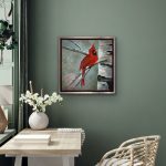 A bright red cardinal sits on slender winter branches beside a textured birch trunk. Soft teal and gray tones form a snowy background with subtle sparkle from mica and glass glitter. The artwork is set in a silver floater frame.