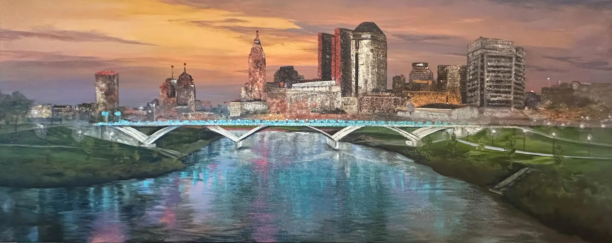 Panoramic mixed-media painting of the Columbus, Ohio skyline at dusk, viewed over the Scioto River with arched bridges and glowing reflections in the water. The artwork features glass and mica sparkle that catches the light, framed in a black floater frame.